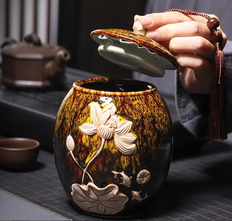 Ceramic tea container with floral designs being opened by a hand.