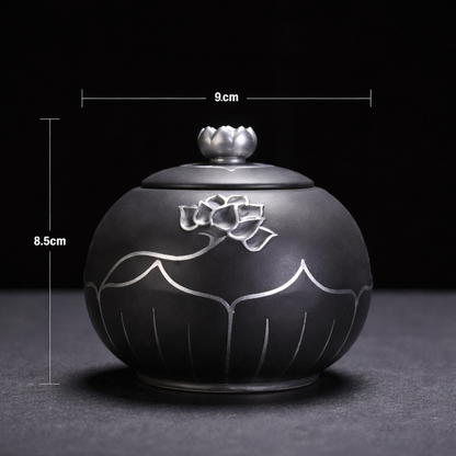 Black ceramic container with silver floral design and lid, shown with measurements on a dark background.