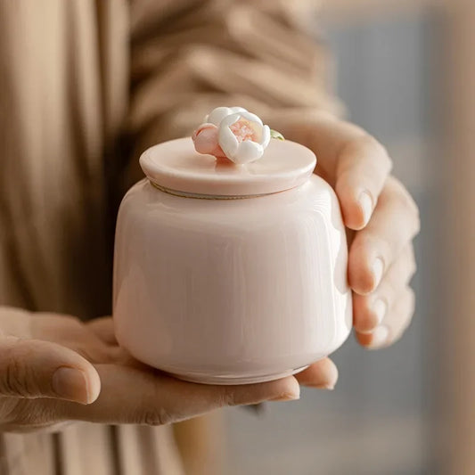 Person holding a small pink ceramic jar with a lid featuring floral designs.